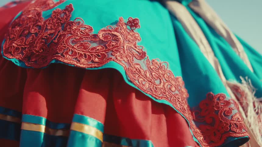 A vibrant red skirt adorned with intricate golden lace detailing against a clear blue sky