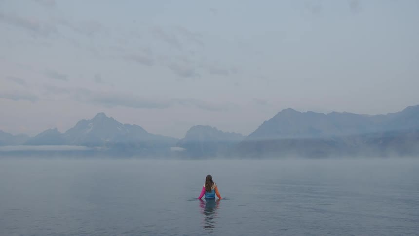 Woman in a calm sea with fog and mountains in the background