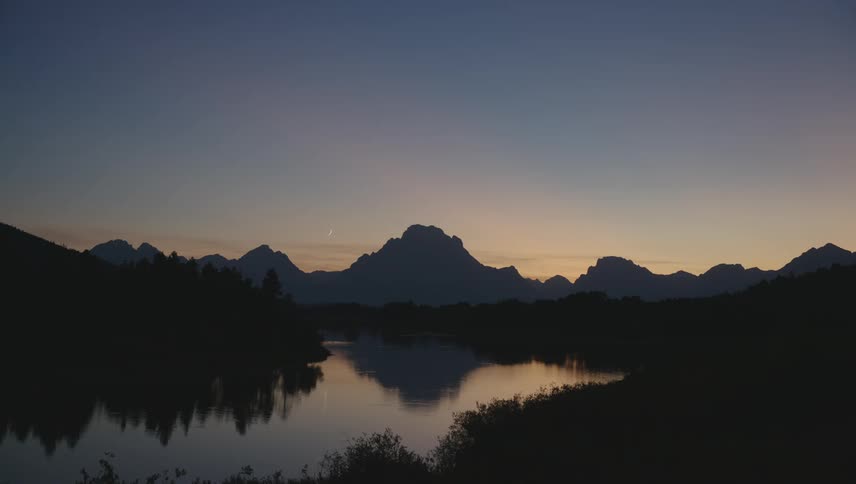 A mountain range silhouetted against a colorful sunset sky reflected in a still lake