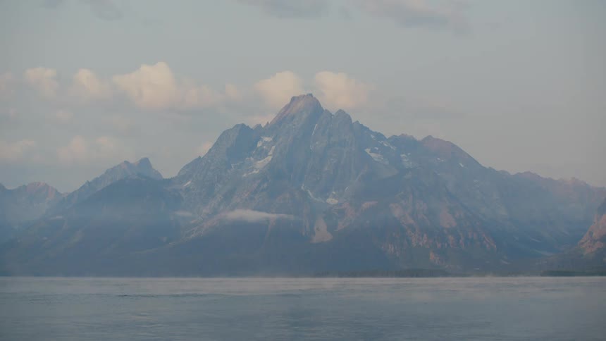 A majestic mountain range with snow capped peaks rises dramatically above a calm body of water