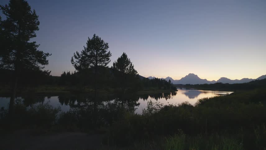 The still water of the lake mirrors the silhouette of mountains against the fading light of dusk