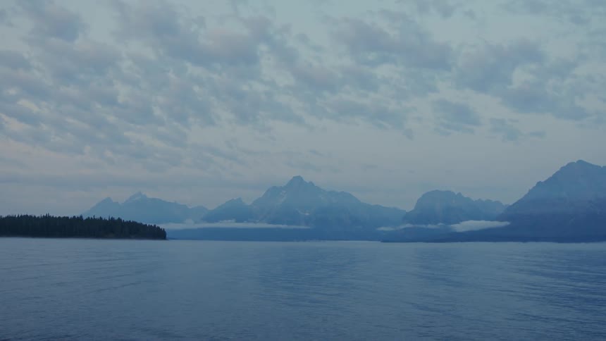 A vast still lake stretches towards a range of mountains shrouded in mist