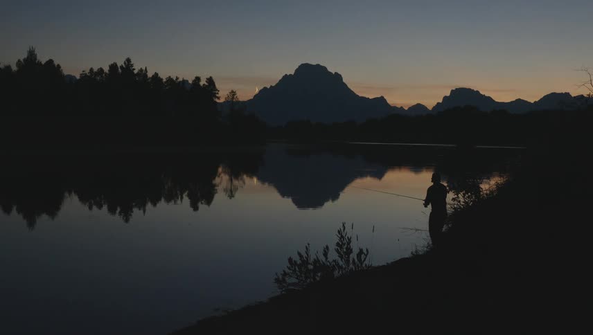 Silhouette of a male fishing lakeside in the wilderness at dawn
