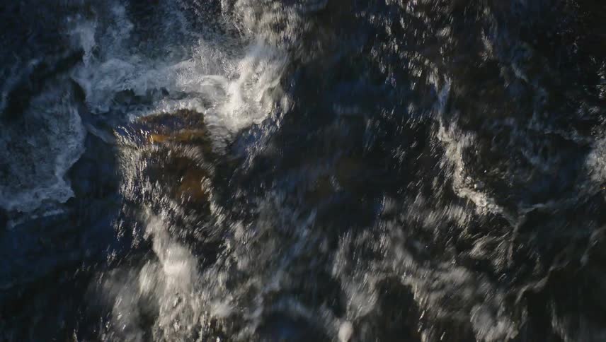 A rushing river with whitewater churning and crashing over dark rocks