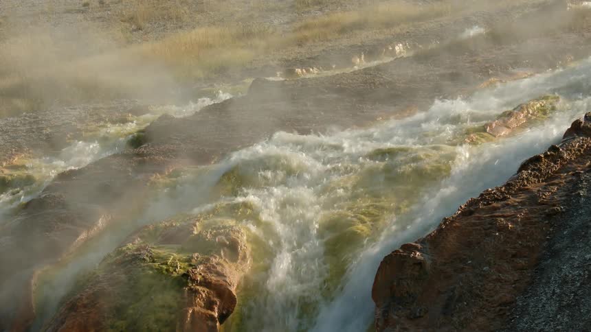 Rapids flow over rocks in a stream as fog rises from the water