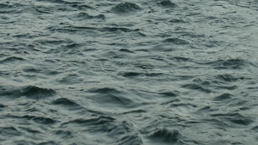 A closeup of a choppy sea surface with dark swirling waves