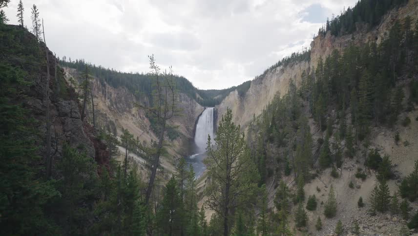 Yellowstone falls pours over a mountain cliff on a mostly cloudy day