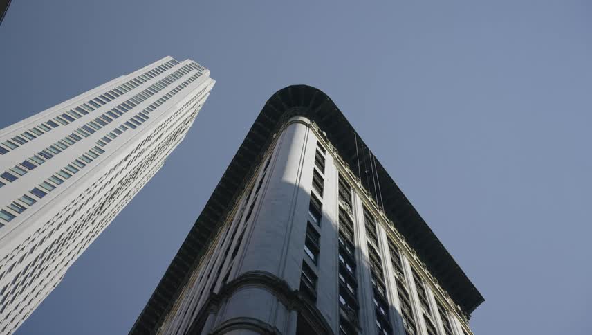A lowangle view of two iconic new york city skyscrapers the slender modern one vanderbilt and the historic rounded corner of 5 columbus circle set against a clear blue sky