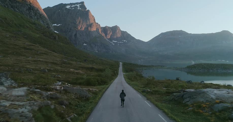 A lone runner making their way down a road with mountains and a still lake