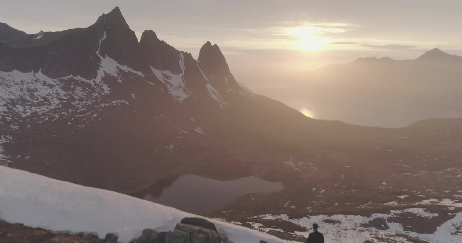 Aerial view of a person walking on a mountain in a snowy valley with the sunrise on the horizon