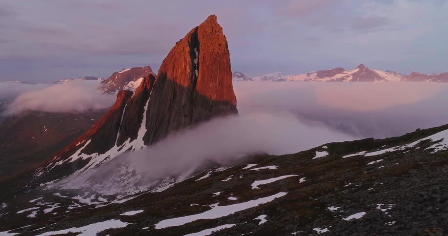 Man stands near the edge of a cliff looking toward a tall rock formation in mountainous terrain on a winter day