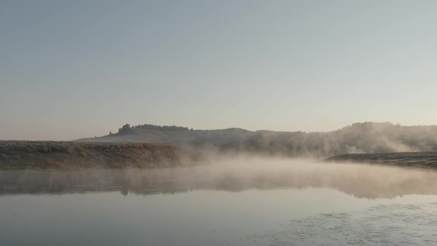 Mist rises from the water and clings to the lowlying hills as the sun begins to rise