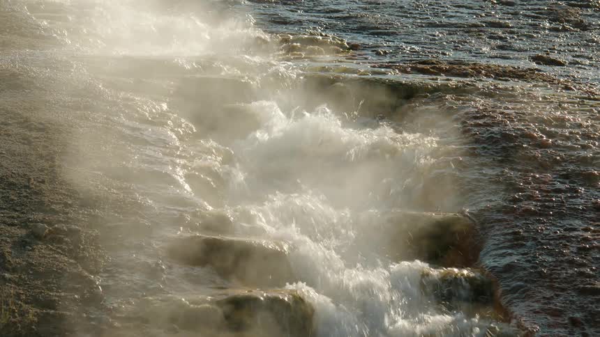 Narrow stream flows down a series of step like ledges on a slope filling the air with vapor