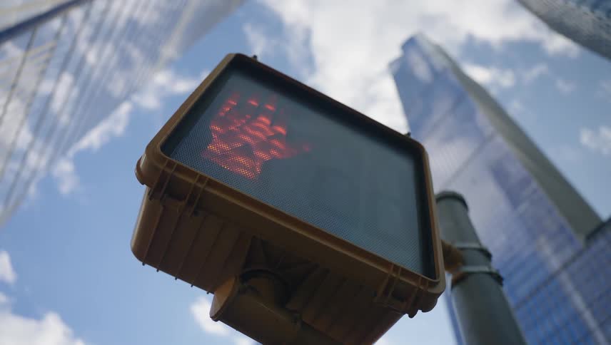 A pedestrian crossing signal is set against tall skyscrapers and a partly cloudy sky