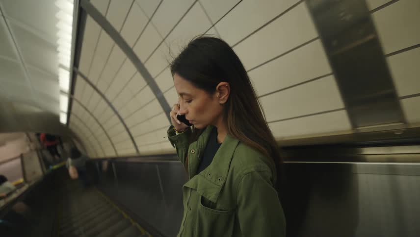 A woman descends a subway escalator while talking on a smartphone