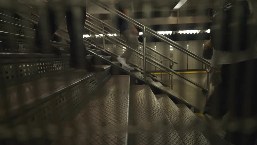 People are walking up and down a set of stairs in a subway station focusing on their legs and feet
