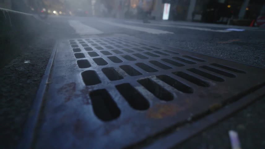 Steam rising from a metal drain grate on a city street