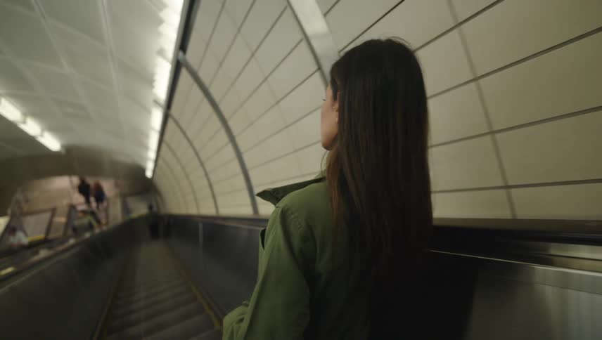 A woman descends a subway escalator while talking on a smartphone