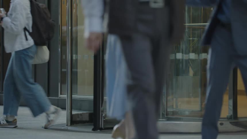 People exit a building through a revolving door onto a busy sidewalk