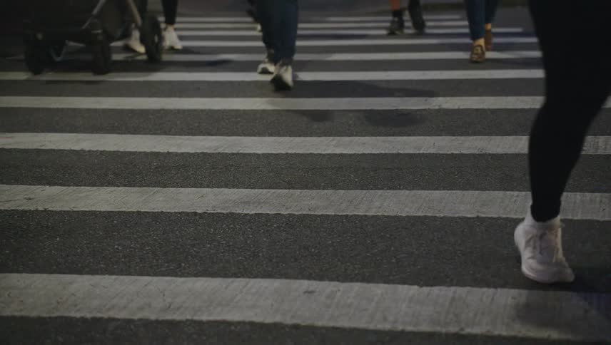 Pedestrians cross the street at a crosswalk after vehicles pass by on the street