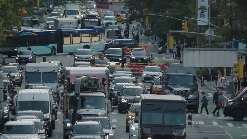 Several cars stopped on a very busy street with some people crossing at the pedestrian crossing