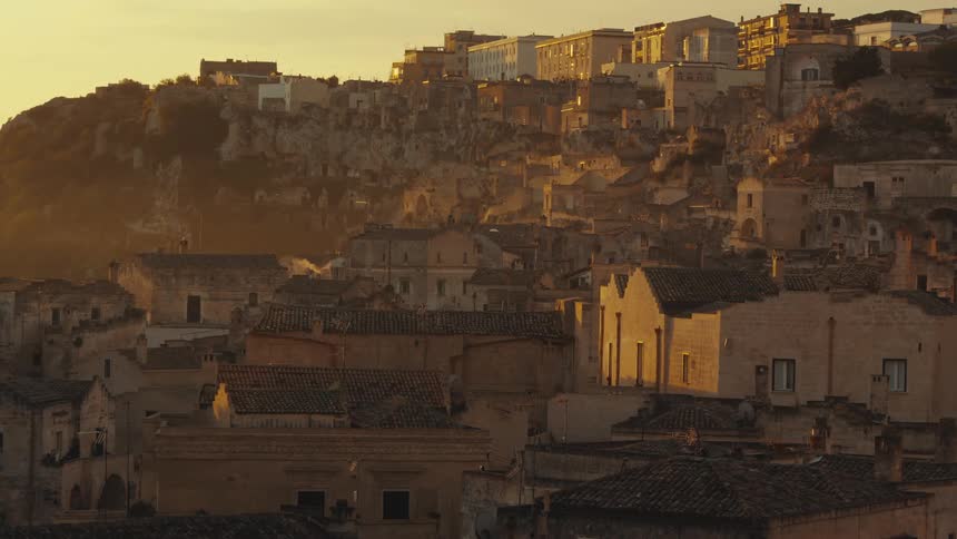 A hillside town at sunset with buildings made of tancolored stone and terracotta roofs nestled into the rocky landscape