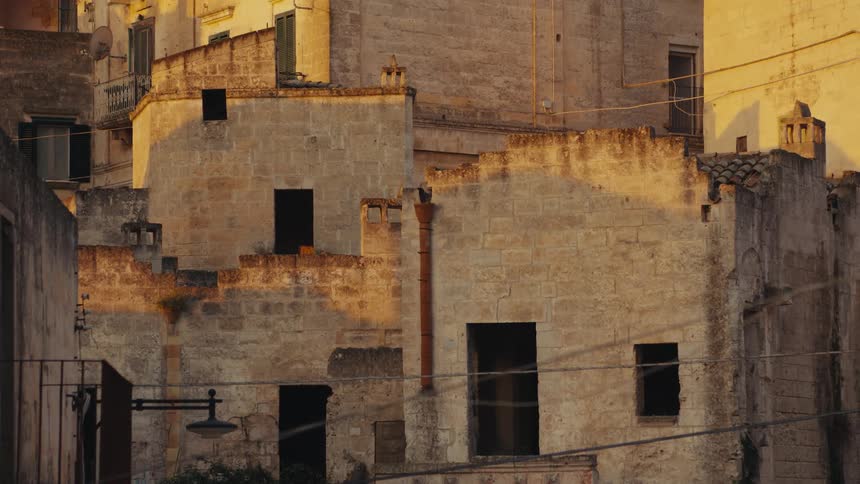 A view of a weathered stone building with several open windows and a cast shadow