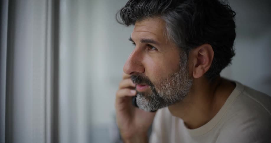 Bearded man wearing a white sweatshirt talks on the smartphone