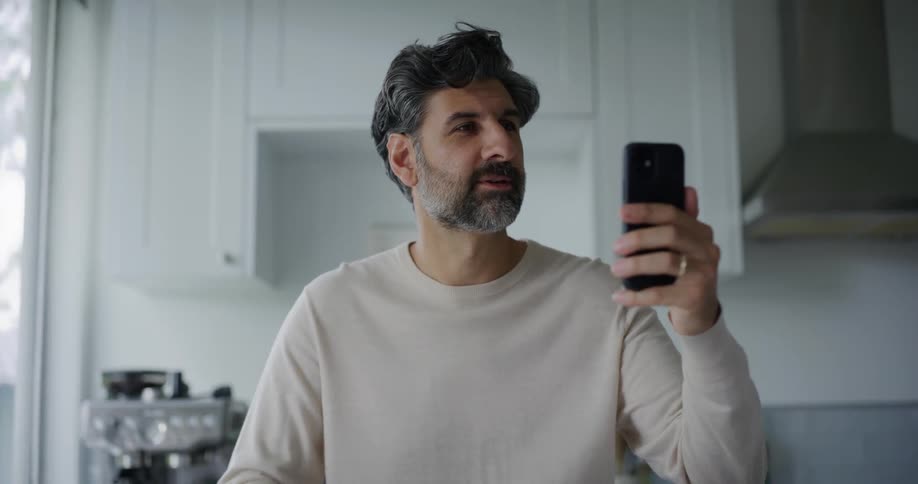 A man answers a video call on his smartphone in the kitchen at home