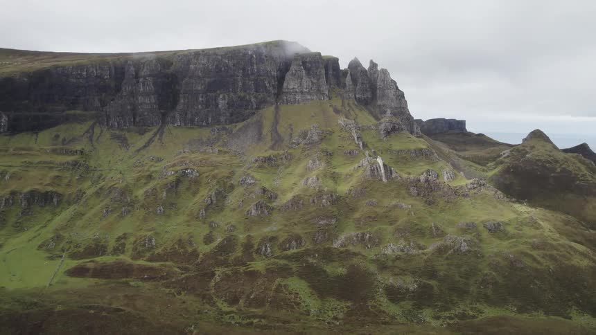 A dramatic landscape of rugged cliffs and rolling hills covered in lush green vegetation stretches towards a cloudy sky