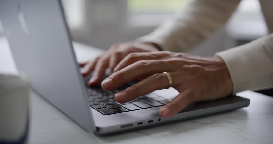A mans hands typing on a laptop keyboard with the focus on their fingers and the keys