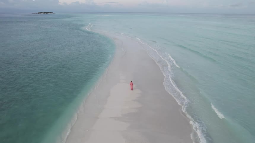 Female is walking on the sandy shore near ocean water