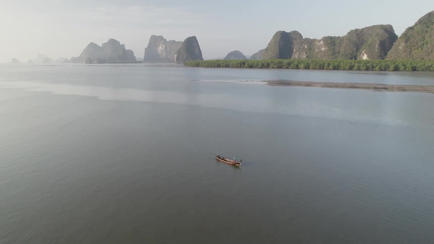 A lone boat floats in the middle of a calm lake near jagged mountains