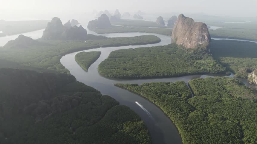 A winding river cuts through a lush green landscape surrounded by dramatic limestone cliffs shrouded in mist