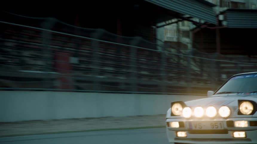White sports car with headlights on racing down a track
