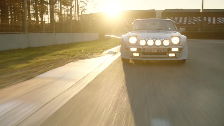 Race car drives along a track near grandstands near sunset