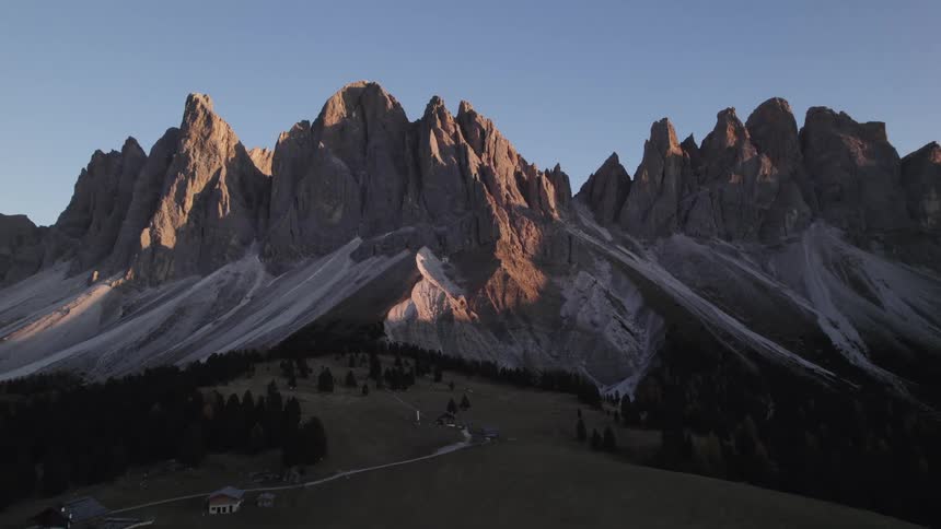 A mountain range with jagged peaks is bathed in the warm light of the setting sun