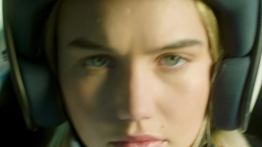 A woman wearing a helmet appears to be in a vehicle moving at a high rate of speed