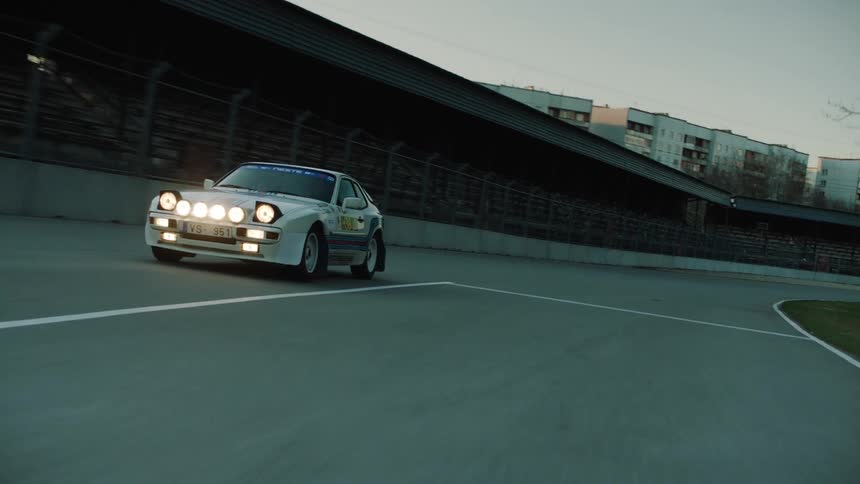 A white race car with its headlights on drives around a racetrack