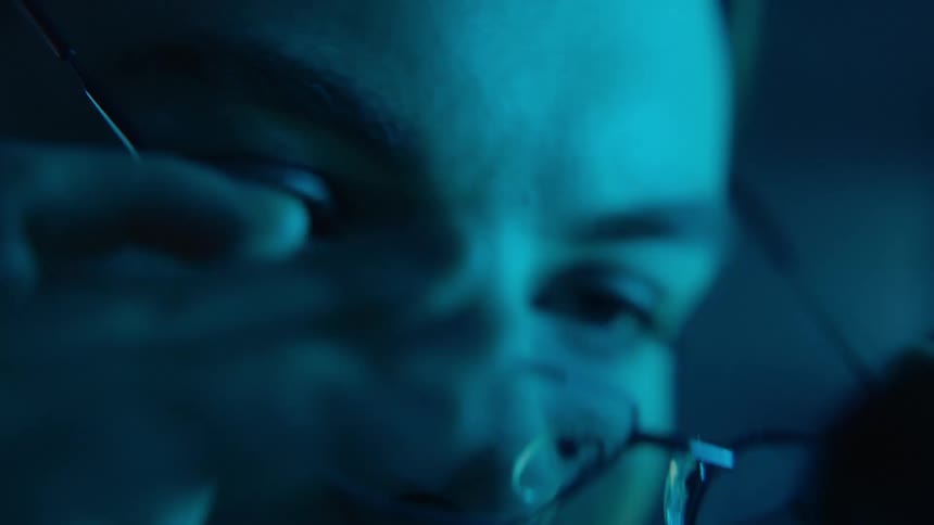 Closeup of a laboratory technician taking off her glasses to rest her eyes before continuing to look through a microscope