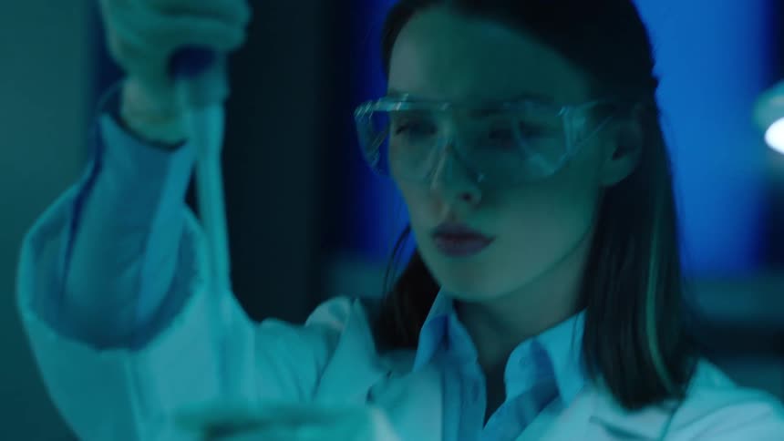 A female lab technician uses a syringe to add clear fluid to a test tube