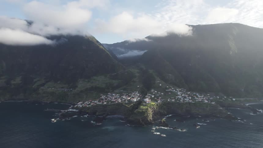 A small coastal village nestled amidst dramatic cliffs and rolling hills with clouds swirling overhead