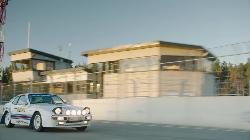 A white sports car with several stickers and headlights on driving on a race track