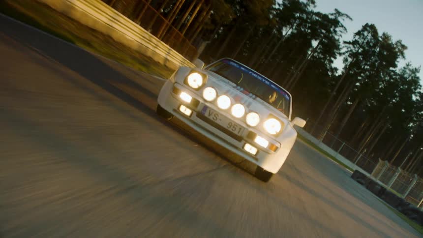 A man drives fast in a car on a road with a forest to the side