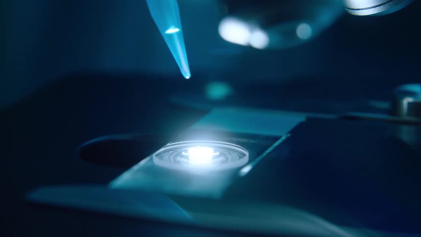 Liquid from a dropper splashes onto a slide on a microscope