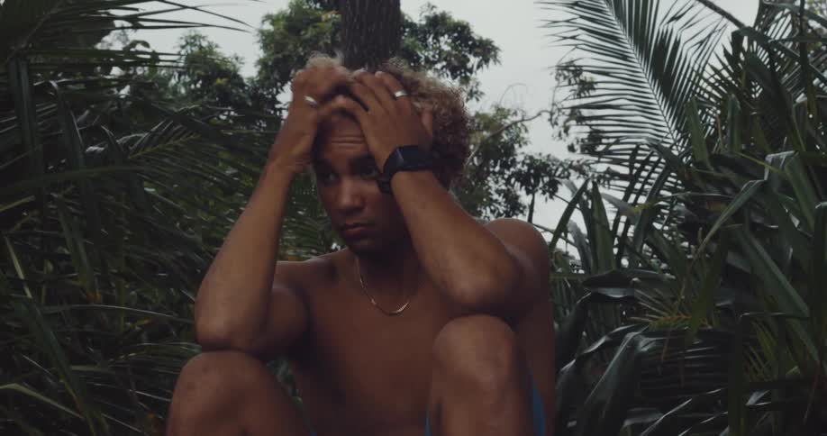 A man sits thinking among plants in a jungle