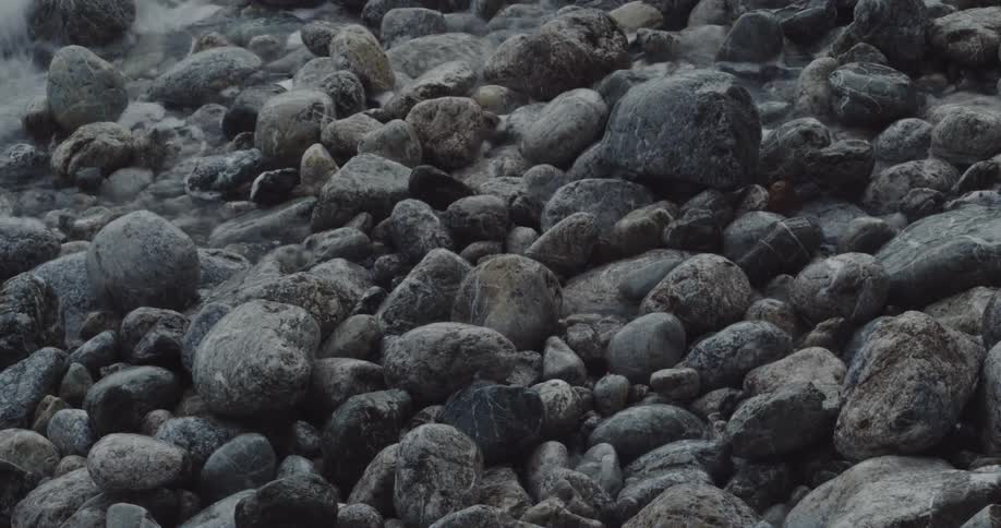 Several circular pebbles on a bet are hit by the foam of a wave that then retreated