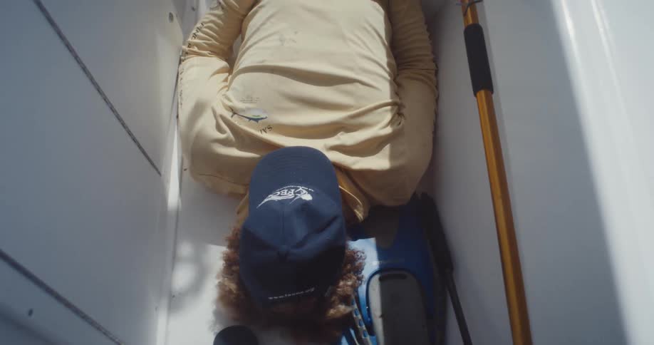 Man with a cap on his face lying on a narrow lane of a moving boat