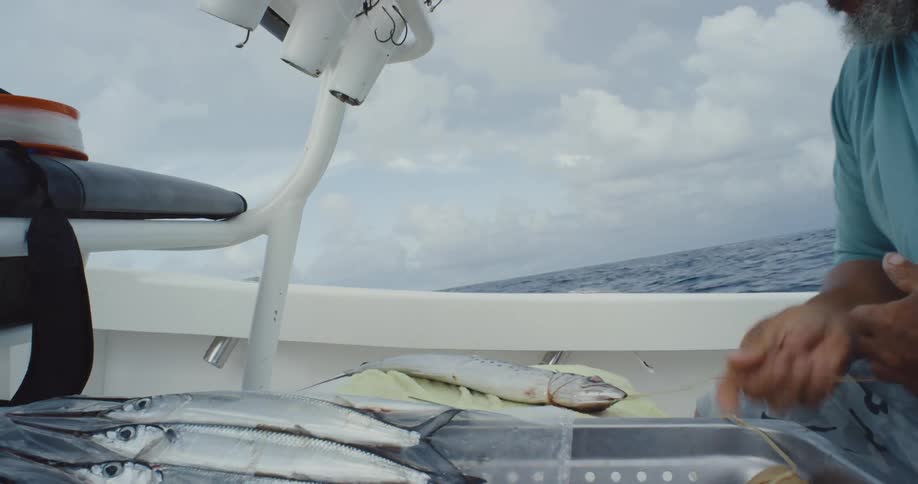 A person is preparing bait on a fishing boat threading a line through a fish