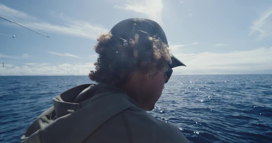 Man sits on a fishing boat bobbing on the ocean under a cloudy sky
